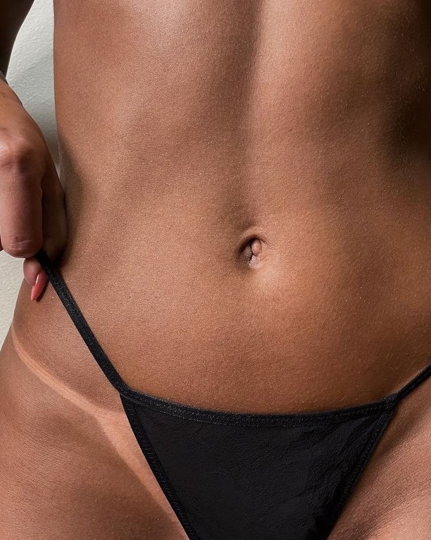 Close-up of a stomach after an AMBREA spray tan, the strap pulled aside to reveal an even golden tan line